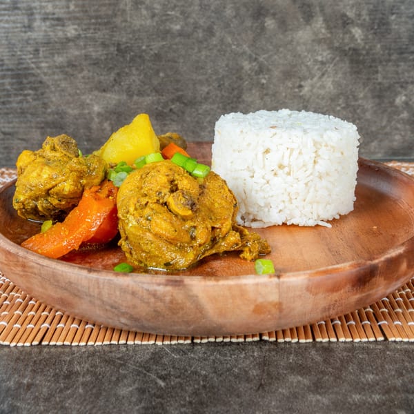 Curry chicken with carrots, potatoes, and white rice on a wooden plate.