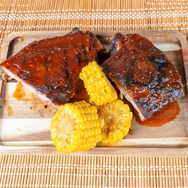 Two pieces of Jamaican jerk ribs with corn on the cob on a wooden tray.