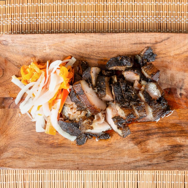 Jamaican jerk pork with sliced onions and bell peppers on a wooden board.