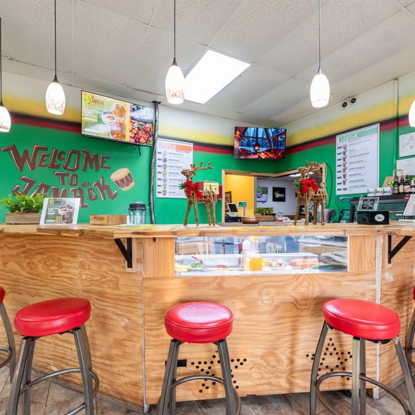 Interior of JAMROK Caribbean Buffet with a wooden counter, red stools, and green walls.