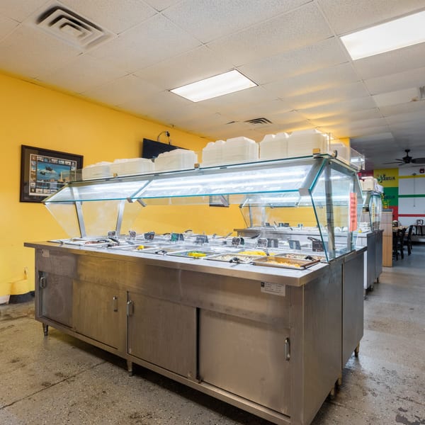 A long, stainless steel buffet line with various Jamaican dishes and stacked takeout containers.