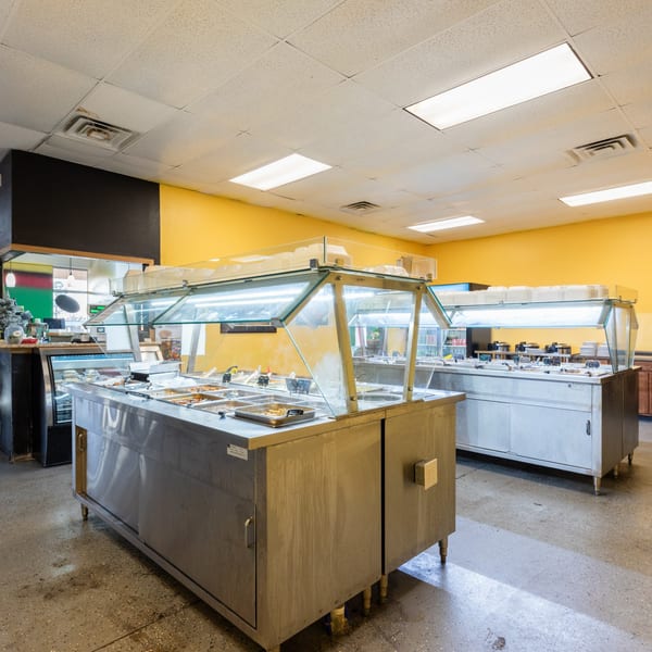 A brightly lit Jamaican buffet line with various dishes in stainless steel warmers and yellow walls.