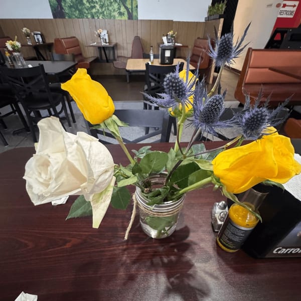 A vase of yellow roses and blue thistles on a dark wooden table in a Jamaican restaurant.