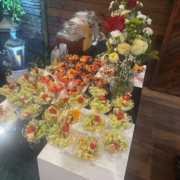 A buffet table with individual servings of salads, fruit cups, and beverages, adorned with flowers.