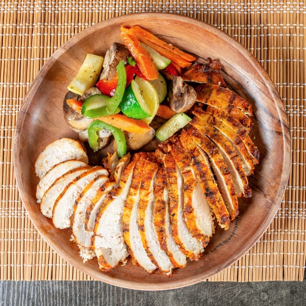 Sliced jerk chicken breast with sautéed vegetables including carrots, zucchini, bell peppers, and mushrooms.