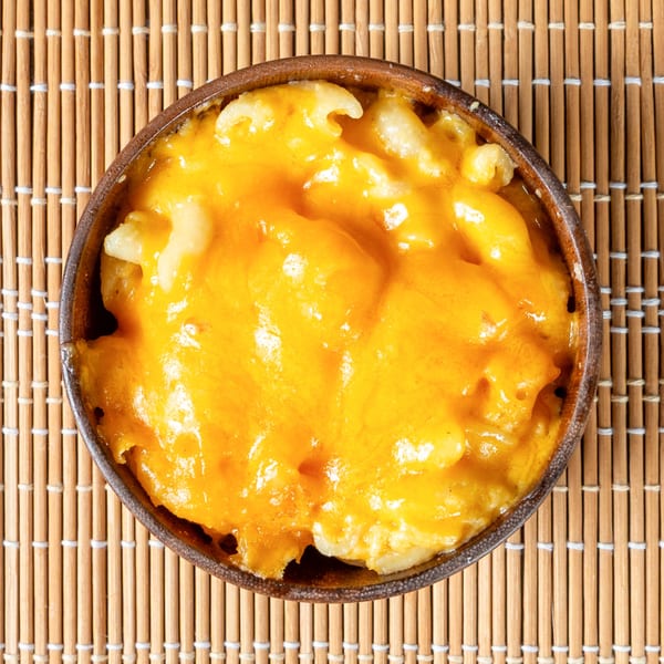 A bowl of Jamaican-style baked macaroni and cheese with a golden-brown cheesy topping on a bamboo mat.