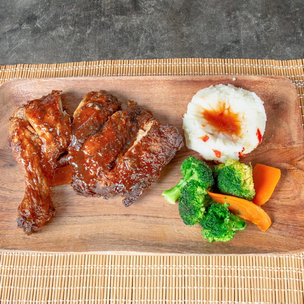 Jamaican jerk chicken with mashed potatoes, broccoli, and carrots on a wooden platter.