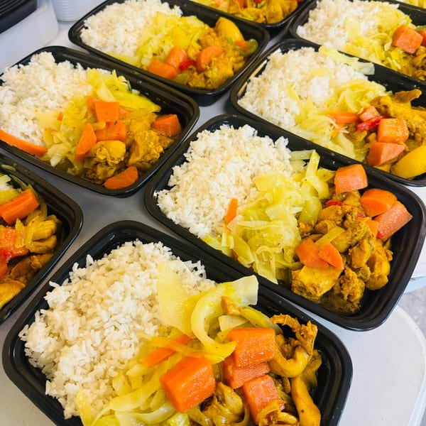 Multiple black containers filled with white rice, yellow curry chicken, and sautéed cabbage and carrots.
